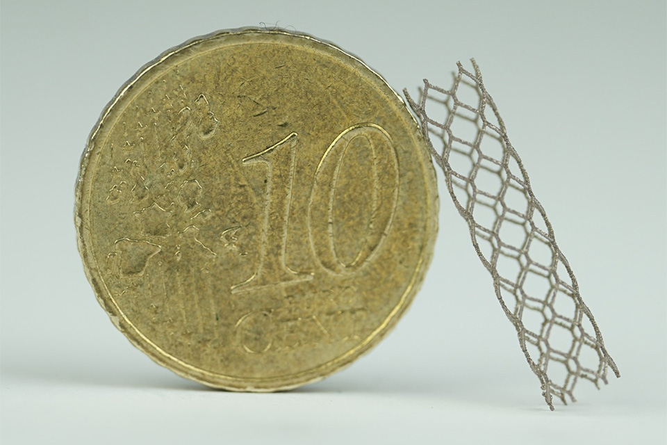 ©Fraunhofer IWU: 3D-gedruckter Stent (Nickel-Titan-Legierung) im Größenvergleich mit einer 10-Euro-Cent-Münze.